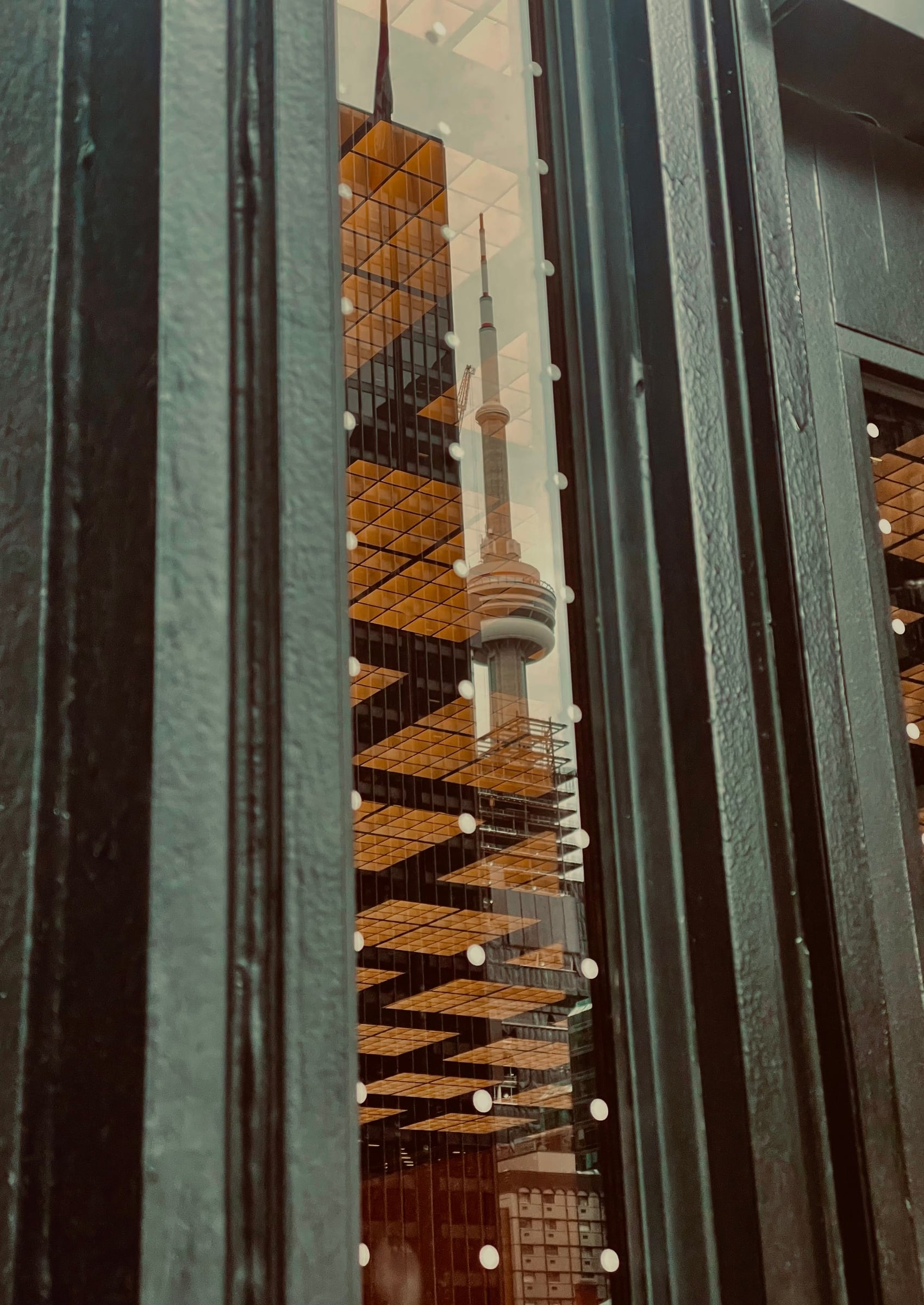 A reflected Toronto tower seen through dark architectural glass and metal.